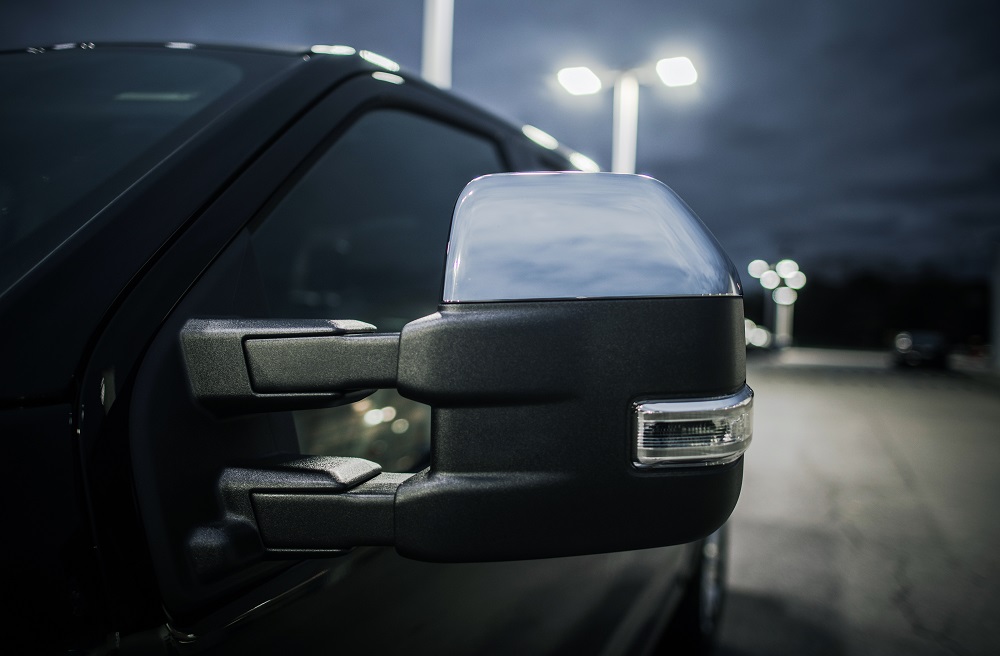 Close-up of a chrome side mirror on a black pickup truck, taken at night in a parking lot with bright overhead lights—showcasing expert window tinting and detailing services in New Orleans.