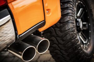 Close-up of the rear end of an orange vehicle in LA, showcasing dual exhaust pipes and a large off-road tire—a standout among Custom Cars in Mandeville.