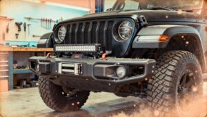 A black off-road vehicle with large tires and a sturdy front bumper is parked in a garage workshop equipped with tools and a workbench, showcasing the expertise of Custom Cars in Kenner.
