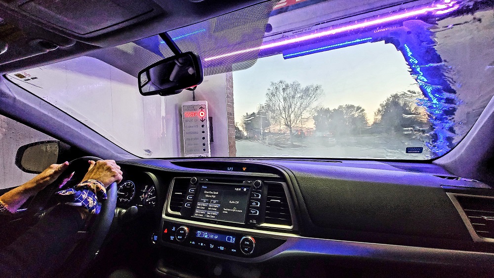 View from inside a car going through an automatic car wash in New Orleans, with hands on the steering wheel and water streaming down the windshield—perfect lighting upgrades make every detail shine.