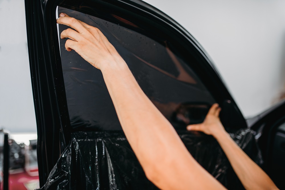 A person applies dark window tint film to a car door window, showcasing professional Window Tinting and Detailing Services in New Orleans.