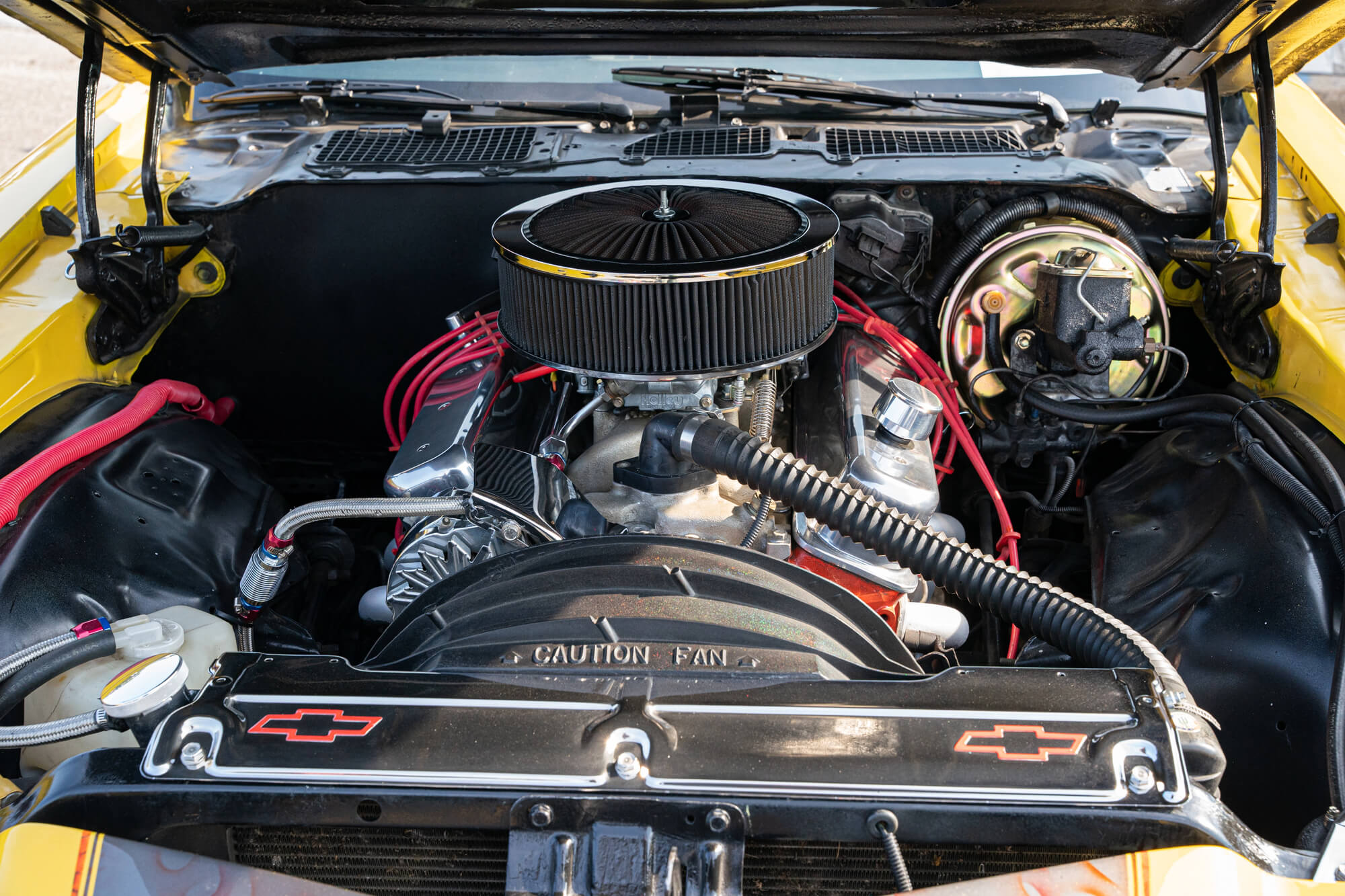 Close-up view of a vehicle's engine bay after an engine tune-up, featuring a prominent air filter, red ignition wires, and the Chevrolet logo on the radiator cover.