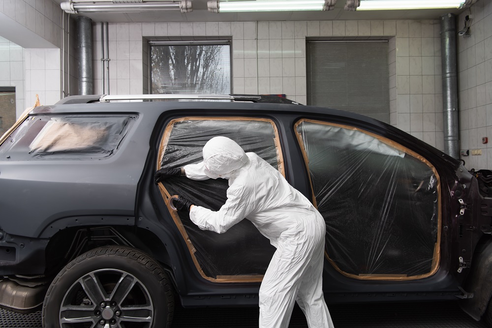 A person in protective clothing prepares a black SUV for painting inside an auto body shop, with windows and trim masked off—showcasing expert Restoration and Rebuilds in New Orleans.