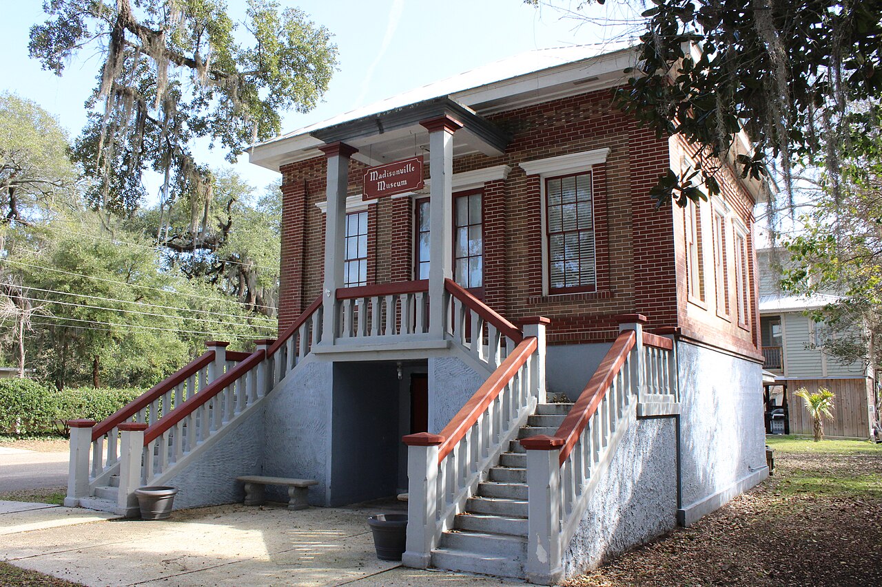 The brick Madisonville Town Hall Museum under live oaks