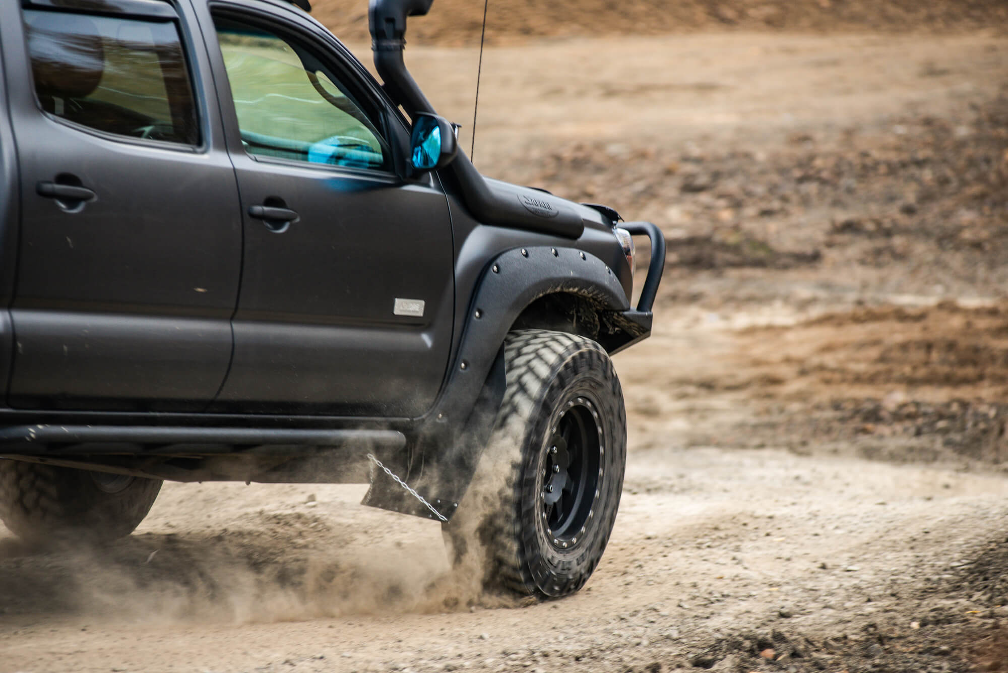 Black lifted pickup kicking up dust on a dirt road